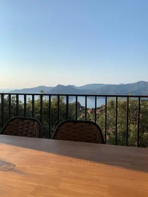 a table and chairs on a balcony with mountains in the background at Appartement spacieux avec vue mer in Piana