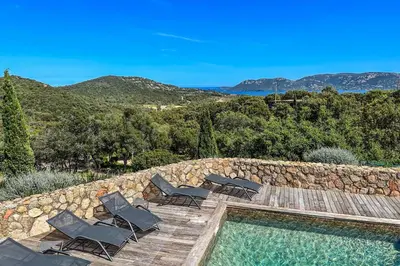 a swimming pool with chairs and a rock wall at Villa Casteddu Di Porto-Vecchio in Porto-Vecchio
