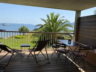 a table and chairs on a deck with a view of the ocean at Les oliviers 6 - Appartement pieds dans l'eau in Porto-Vecchio