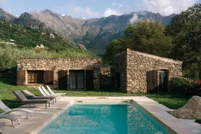 a swimming pool in front of a stone building with mountains at Domaine Acciola in Feliceto