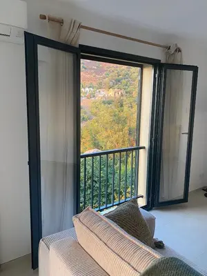 a room with a large window with a couch and a balcony at Grande maison à Belgodère Balagne in Belgodère