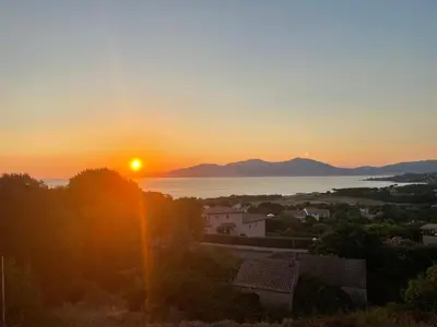 a sunset over the water and a town with the sun at Villa vue mer piscine in Pietrosella
