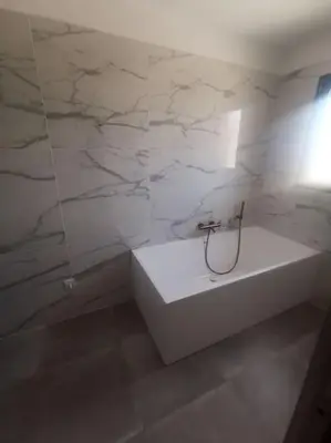 a bathroom with a white tub and marble wall at Villa t4 in Lucciana