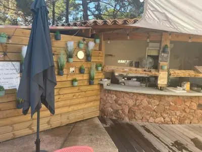 an outdoor kitchen with a stone wall and an umbrella at Corse du sud Fiori di cala rossa T2 rez de jardin dans résidence piscine in Lecci