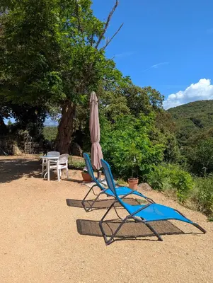 two chairs and an umbrella next to a table and a table and chairs at La chambre de Ptitruc au coeur du maquis in Granace