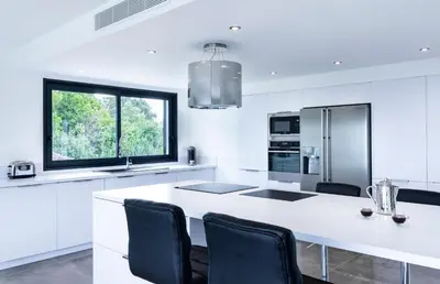 a white kitchen with a large white island with black chairs at a STELLA DI FOCE in Kamiesch