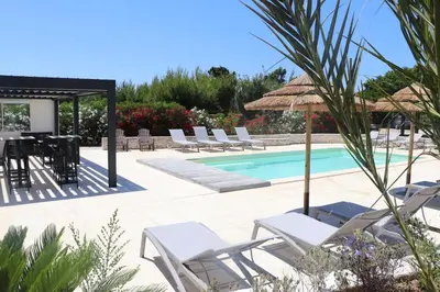 a swimming pool with chairs and a table and an umbrella at Hôtel Padolo in Bonifacio