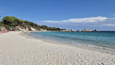 a beach with people sitting on the sand and the water at Villa Nitiola Plage de Palombaggia in Bocca del Oro