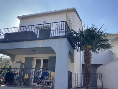 a white house with a palm tree in front of it at Appartement Bavella in Santa-Lucia-di-Moriani