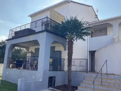 a white house with a palm tree in front of it at Appartement Bavella in Santa-Lucia-di-Moriani