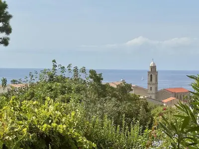 a church on a hill with the ocean in the background at Maison Les aloes - vue mer et proche centre ville in Propriano