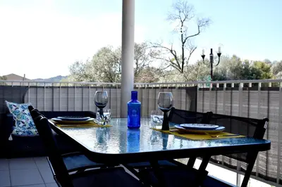 a table with wine glasses and a blue bottle on a balcony at Studio Terrasse entre ville et port in Porto-Vecchio