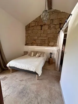 a bedroom with a bed with a stone wall at Maison cantonnière in Sartène