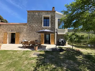 a stone house with a table and an umbrella at Maison cantonnière in Sartène