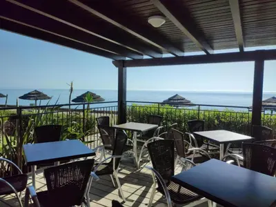 a patio with tables and chairs with the ocean in the background at Appartement dans résidence avec piscine et plage privées in San-Nicolao