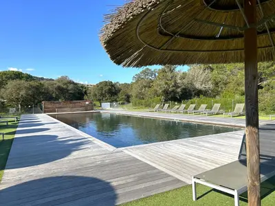 a wooden deck with an umbrella and a swimming pool at Appartement 4 étoiles piscine et plage à pied in Porto-Vecchio