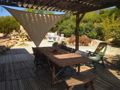 a wooden table and chairs under a wooden pergola at Cottage bergerie en pierres avec jacuzzi en corse 6 personnes, 3 chambres in Coti-Chiavari