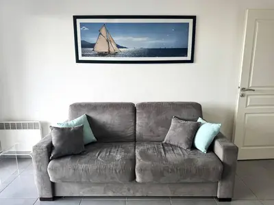 a couch in a living room with a sail boat on the wall at Appartement avec vue imprenable sur la mer, terrasse et piscine in Propriano
