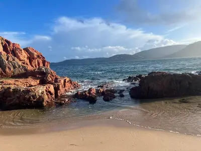a beach with rocks and the ocean with mountains at Location T2 44 m2 proche plage Lecci appartement 82 in Lecci