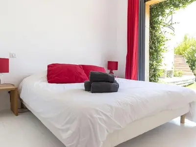 a bedroom with a white bed with red pillows and a window at Villa Palombaggia in Porto-Vecchio