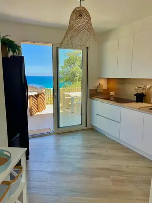 a kitchen with white cabinets and a view of the ocean at Maison Bord'eau in Sainte-Lucie de Porto-Vecchio