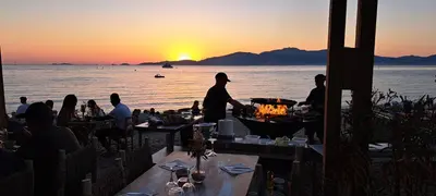 a group of people sitting at tables in front of a sunset at Duplex neuf T3 terrasse et jardin proche plages in Pietrosella