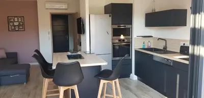 a kitchen with black cabinets and black chairs and a counter at Duplex neuf T3 terrasse et jardin proche plages in Pietrosella