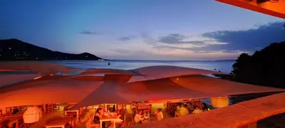 a group of tables with umbrellas in front of the water at Duplex neuf T3 terrasse et jardin proche plages in Pietrosella