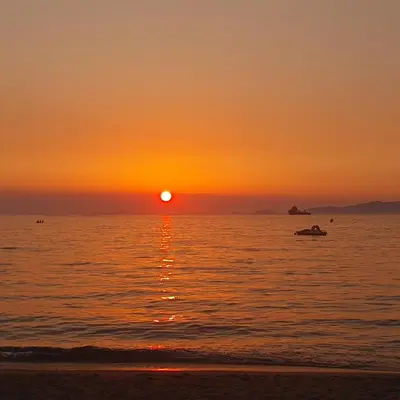 a sunset on the beach with a boat in the water at Duplex neuf T3 terrasse et jardin proche plages in Pietrosella