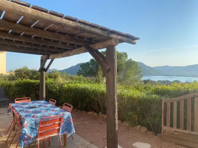 a table and chairs under a wooden pergola at Villa vue mer exceptionnelle à 500m de la plage de Santa Giulia in Porto-Vecchio
