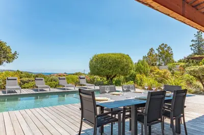 a dining table and chairs on a deck next to a pool at Casa Di Sole Di Pinarello in Pinarellu