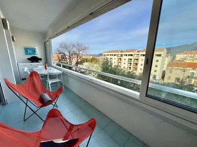 a balcony with two red chairs and a table and a window at Appartement vue sur les toits de Propriano in Propriano