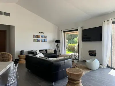 a living room with a black couch and a tv at Villa en pierre avec piscine chauffée, à proximité des plus belles plages du sud de la Corse ! in Figari