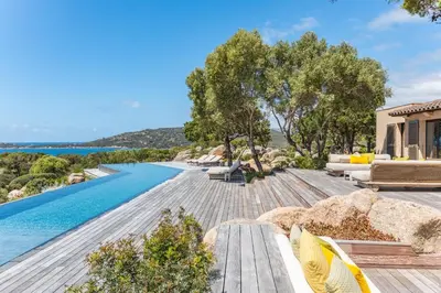 an infinity pool with chairs and a house at Casa Rocca Di Pianotolli in Pianottoli-Caldarello
