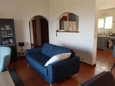 a living room with a blue couch and a kitchen at Villa Abbracciu climatisée avec piscine chauffée et vue mer in Pietrosella