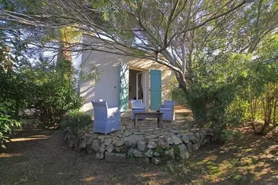 a house with two chairs and a table in front of it at Villa Abbracciu climatisée avec piscine chauffée et vue mer in Pietrosella