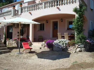 a house with an umbrella and chairs and flowers at Appartement Appietto in Appietto