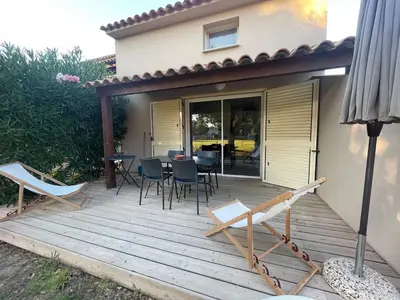 a wooden deck with chairs and tables in front of a house at Mini villa avec jardin Cala Rossa - Porto Vecchio in Lecci