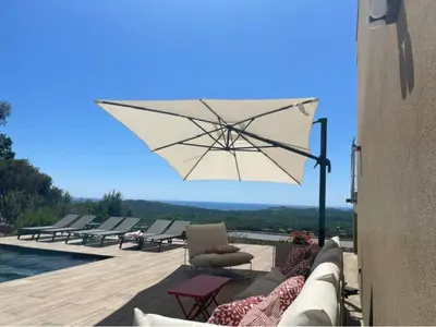 a patio with a white umbrella and chairs and a pool at family villa, beautiful open sea view & scrubland in Conca