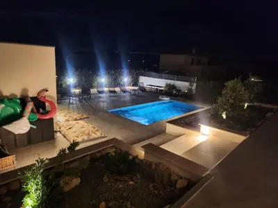 a person sitting on a bench next to a swimming pool at night at Villa DIMA - piscine chauffée climatisation barbecue pétanque in Calenzana