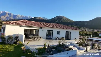 a white house with mountains in the background at Villa DIMA - piscine chauffée climatisation barbecue pétanque in Calenzana