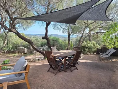 a wooden table and chairs under a black umbrella at I Caselli, mini villa Vue Mer dans résidence calme et arborée in Lecci
