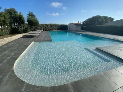 a large swimming pool with blue water in a yard at Villa résidence avec piscine chauffée Bonifacio in Bonifacio