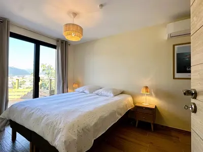 a bedroom with a bed and a large window at Superbe vue Mer et Montagne - T3 - 5mn des plages in Propriano