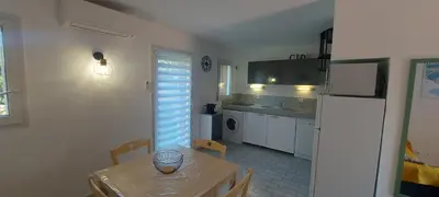a kitchen with a table and a white refrigerator at Porto Vecchio - Résidence RIVIERA- Villa Santa Giulia in Lecci