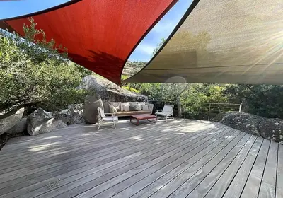 a deck with a couch and chairs under a large umbrella at Villa Cazélie, piscine vue splendide sur le Golfe in Porto-Vecchio