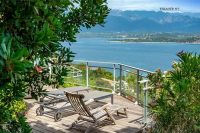 a deck with two chairs and a table and the ocean at Les Hauts de Pavellone in Porto-Vecchio