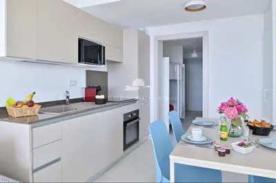 a kitchen with white cabinets and a table with blue chairs at Résidence Eden Suites in Ajaccio