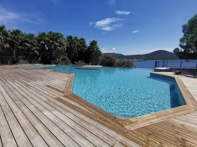 a swimming pool with a wooden deck and water at Le Loria - T3 vue mer avec piscine in Pianottoli-Caldarello