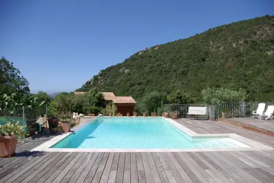 a swimming pool with a wooden deck and a mountain at Chambres d'Hôtes Littariccia in Porto-Vecchio